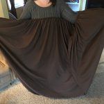 person in gray sweater holding brown fitted bed sheet in front of her. One end of sheet in each hand