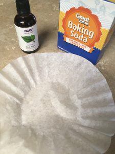 Coffee filter, tea tree oil, and baking soda sitting on a counter
