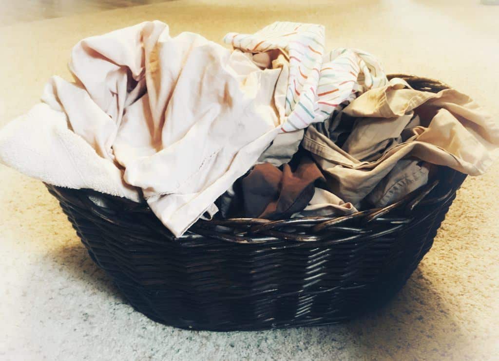 Brown wicker laundry basket with a pile of sheets in it on a ivory carpet