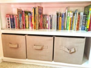 books on a white wooden built in book shelf with fabric storage totes on bottom shelf