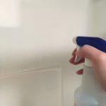 Hand holding a spray bottle spraying a shower wall.