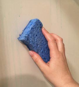 Hand holding a sponge wiping a shower surround